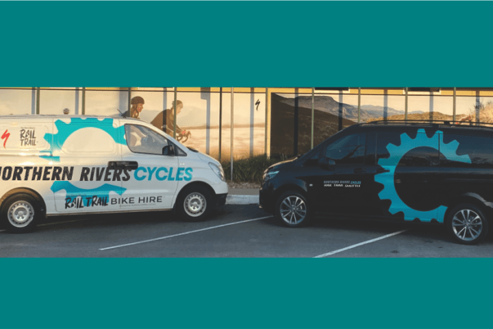 Two branded vans parked, one white and one dark, with cycling-themed graphics.