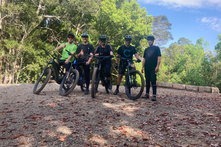 Five cyclists in helmets and gear posing on a gravel path in a forest clearing.