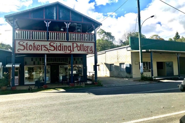 Historic pottery building with 'Stokers Siding Pottery' sign and nearby structures on a sunny day.
