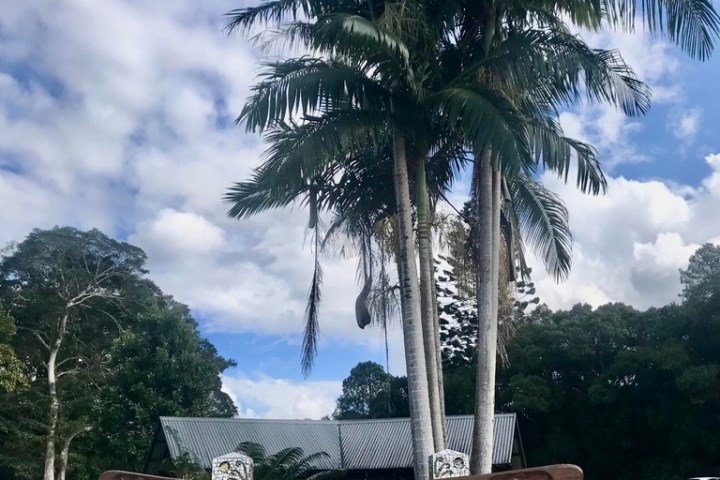 Wooden sign reading 'Burringbar' with palm trees and cloudy sky in background.