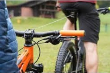 Two cyclists on mountain bikes, one in focus, standing outdoors on grass.