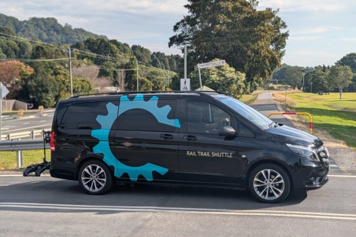 Black van with a large blue gear logo and 'Rail Trail Shuttle' text parked on a road.
