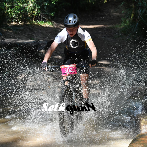 Cyclist splashing through water, wearing helmet and numbered bib 302.