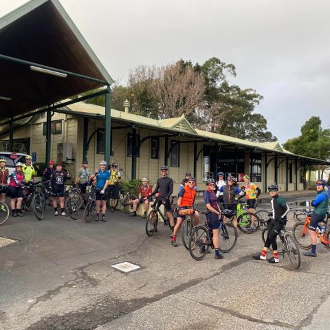 Group of cyclists gathered with bikes outside a building under gray sky.