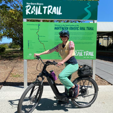 Person on a black bicycle in front of Northern Rivers Rail Trail sign.