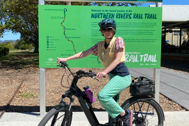 Person on a black bicycle in front of Northern Rivers Rail Trail sign.