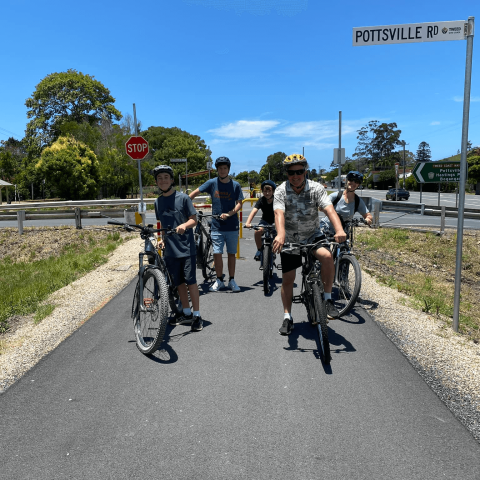 Group of cyclists on a path next to Pottsville Rd sign under blue sky.