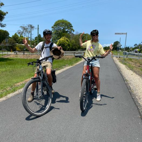 Two cyclists smiling on a paved path, posing with their bikes.