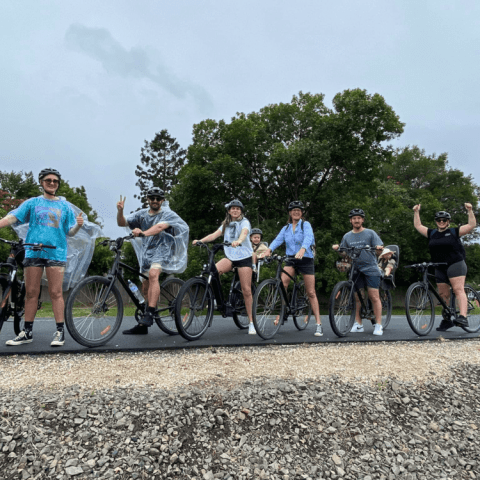 Group of six people with bikes and ponchos posing on a road with trees in the background.