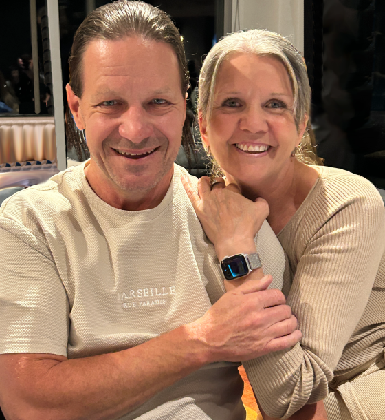 Jeff_Rachel Smiling couple sitting closely, woman wearing a smartwatch, indoors.