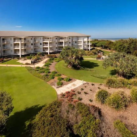 View of a white apartment building with green landscaped gardens and clear blue sky.