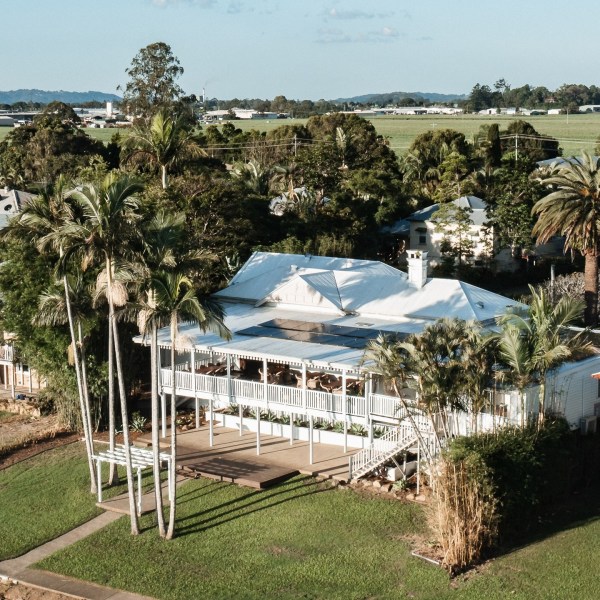 Aerial view of a white house with a veranda surrounded by palm trees.