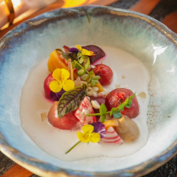 Colorful dish in blue bowl with vegetables, edible flowers, and cream sauce.