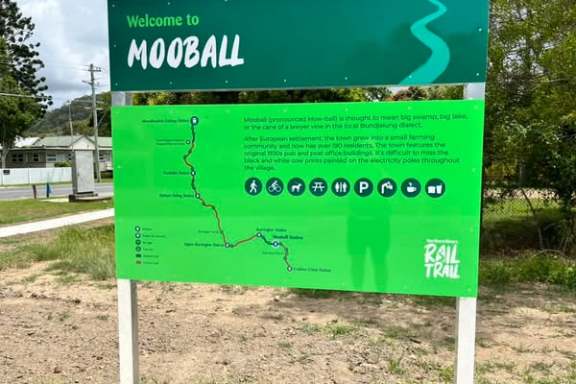 Signboard with 'Welcome to Mooball' and a map of the Rail Trail in a park setting.