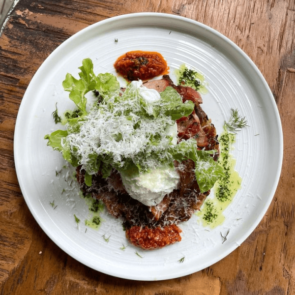 Plate of food with greens, grated cheese, poached egg, and sauce on a wooden table.