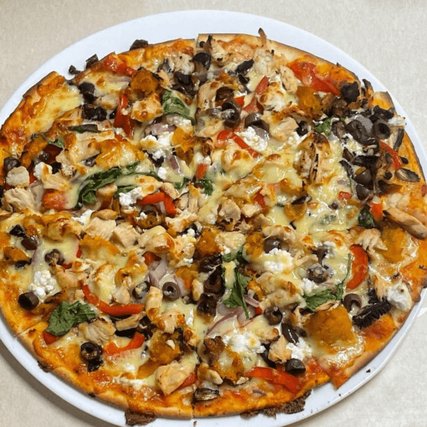 Pizza with assorted toppings including olives, chicken, spinach, and peppers on a white plate.