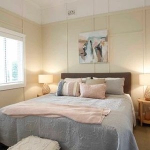 Cozy bedroom with a bed, pillows, lamps, and abstract art on the wall.