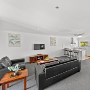 Modern living room with black sofas, TV, kitchen area, bar stools, and wall art.