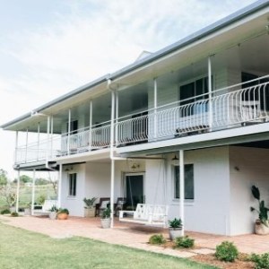 Two-story house with a balcony, white exterior, and garden view.
