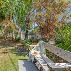 Wooden bench with striped blanket and hat in a sunny garden with palm trees.