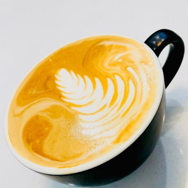 A black cup of cappuccino with intricate latte art on a white surface.