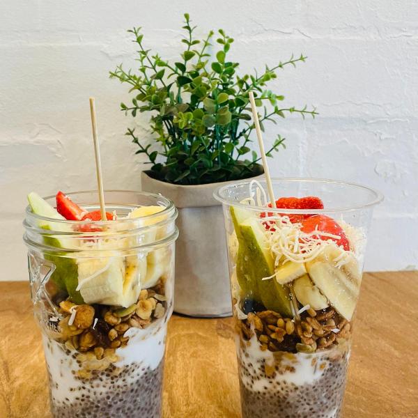 Two chia pudding parfaits with fruits and granola in jars, plant in background.