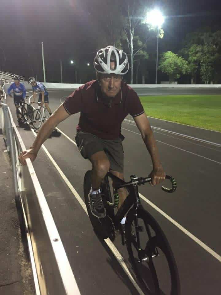 Cyclist in helmet and maroon shirt on a track at night with two other cyclists nearby.