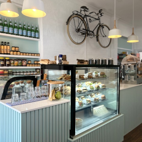 Cafe interior with sandwiches in display, shelves of bottles, and a bicycle decoration on the wall.