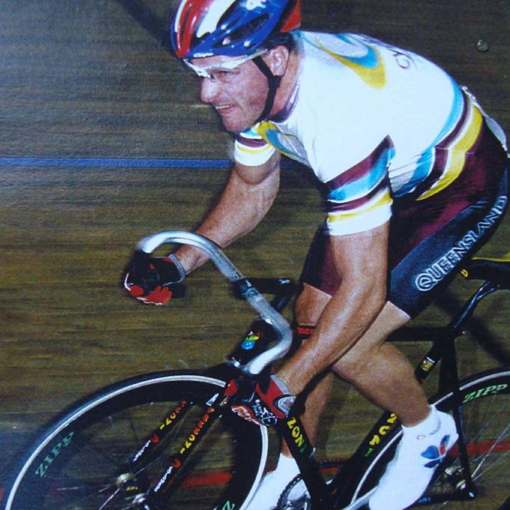 Cyclist wearing colorful gear and helmet racing on an indoor track.