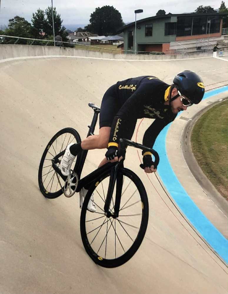 Cyclist in black gear riding on a velodrome track curve.
