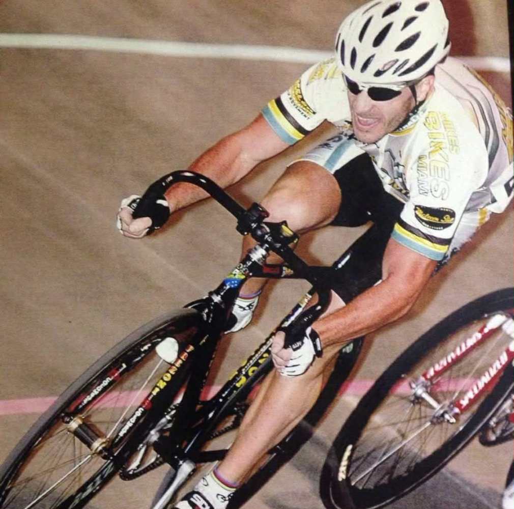 Cyclist in helmet and sunglasses racing on a velodrome track.