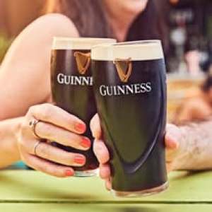 Two hands holding pints of Guinness with creamy heads, cheersing at a table.