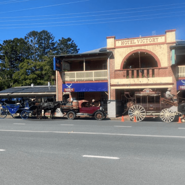 Historic hotel with horse-drawn carriages and vintage car parked in front under a clear blue sky.